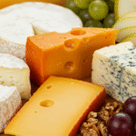 Kolorowa deska serów z różnorodnymi serami, owocami, orzechami i świeżymi ziołami, ukazana z bliska.