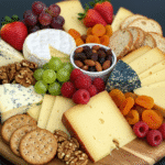 Kolorowa deska serów z różnorodnymi rodzajami serów, świeżymi owocami, takimi jak winogrona, figi i jabłka, oraz orzechami i miodem, podana na drewnianej desce.