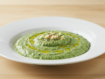 ALT: Sos szpinakowy w miseczce, ozdobiony gałązką świeżej bazylii, podany obok makaronu i posypany parmezanem, na drewnianym blacie kuchennym.